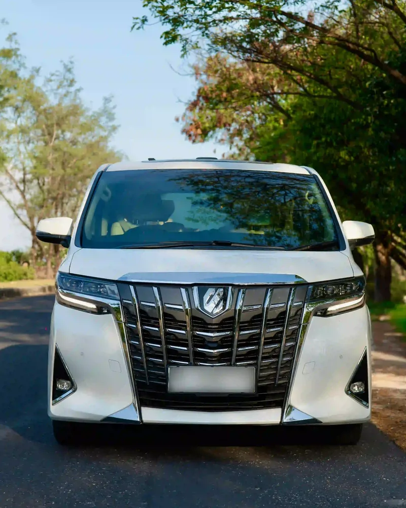 White Toyota Alphard parked on a tree-lined road in Bali