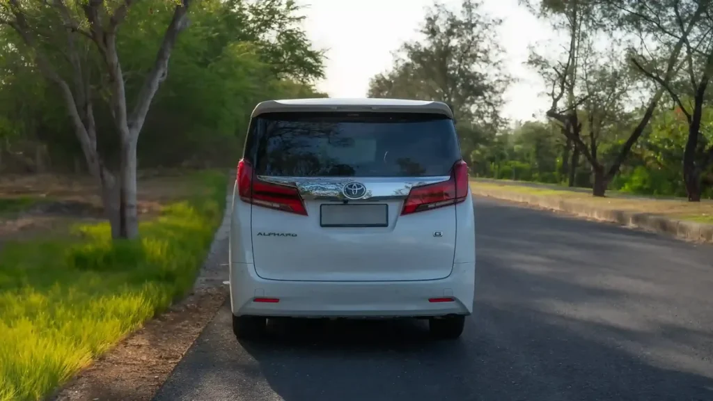 Rear view of a white Toyota Alphard on a tree-lined road