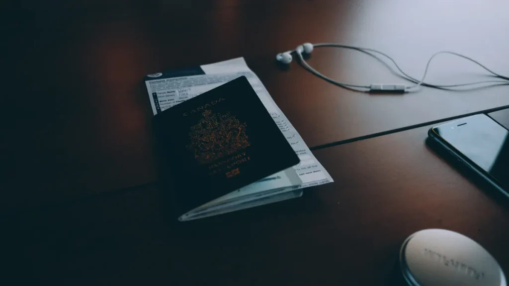 Passport tucked into a boarding pass on a wooden desk next to earphones and a smartphone