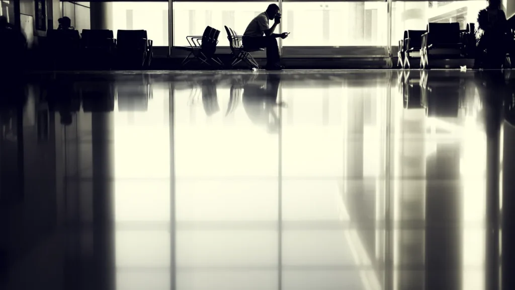 Lone traveller silhouetted in a quiet airport gate area by tall windows